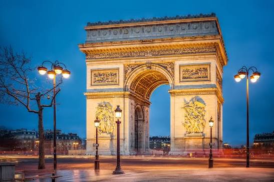 Façade de l'Arc de Triomphe illuminée au crépuscule avec les lampadaires de la place de l'Étoile